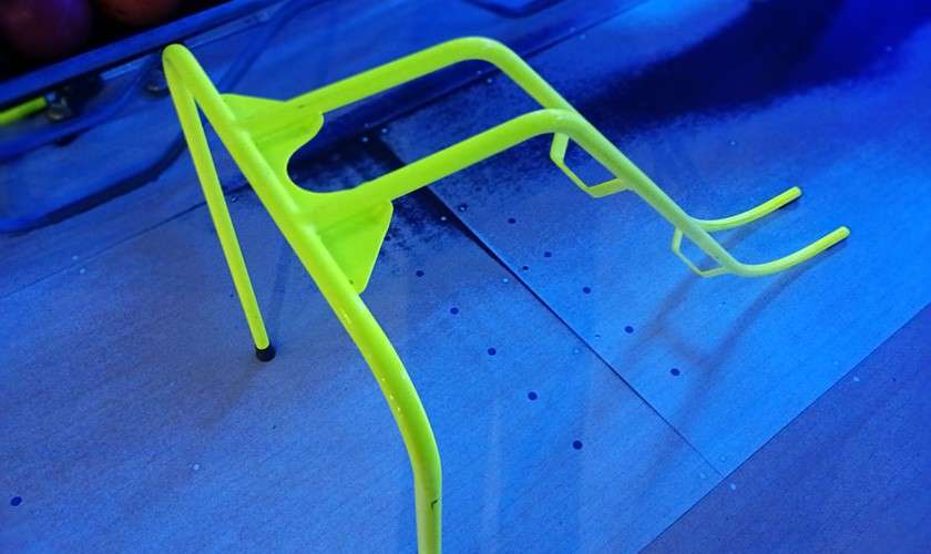 Neon yellow bowling ramp stands on a lane, angled for rolling balls. Context: blue-lit bowling alley surface with lane arrows and gutters nearby.