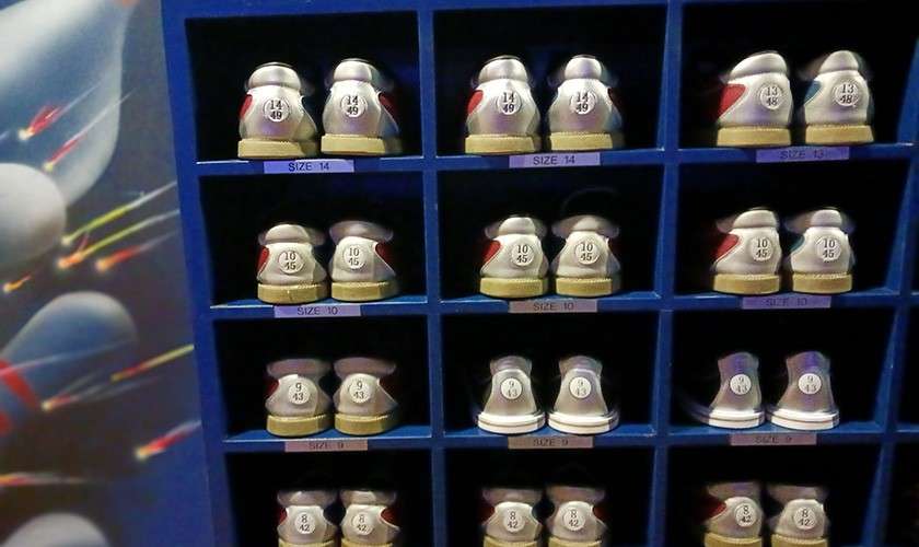 Bowling shoes sit paired on blue cubby shelves, organized by size at a rental counter. Text: SIZE-14, SIZE-13, SIZE-10, SIZE-9. Heel stamps include 14 49, 13 48, 12 47, 10 45, 9 44, 8 43.
