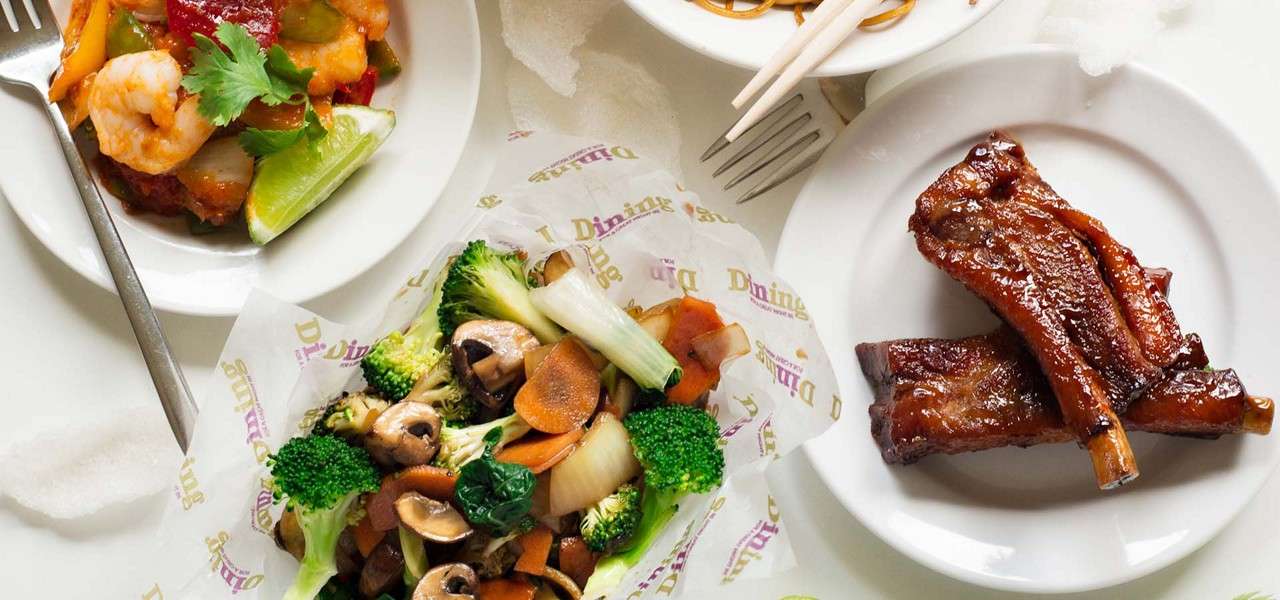 Plates of Chinese-style dishes sit on a white table: glazed pork ribs, shrimp with peppers and lime, noodles near chopsticks, and a paper-lined basket of broccoli, mushrooms, and carrots. Text: Dining (repeated).