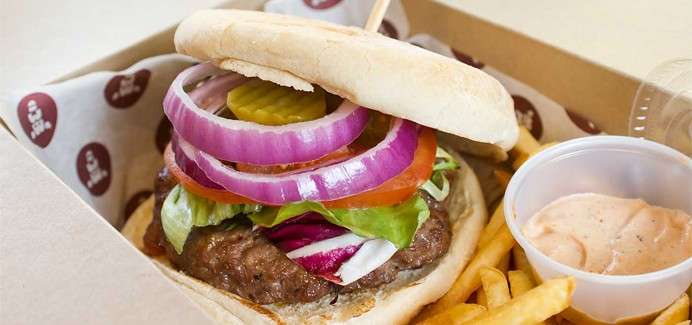 Burger topped with salad and a soft bun served with fries and a dip.