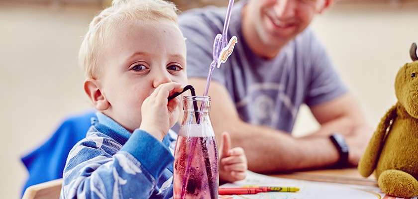 Little boy drinking his drink through a straw and father smiling at him