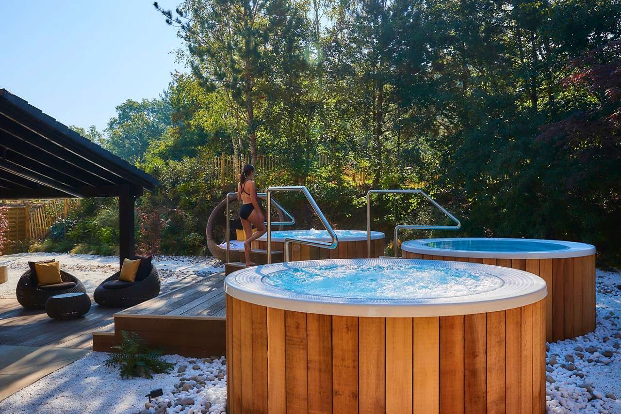 a wooden hot tub outside with forest trees in the background