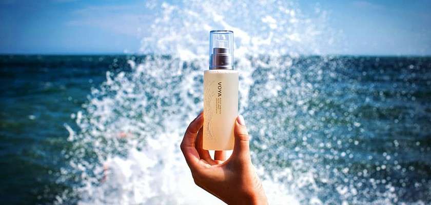 Bottle of VOYA product being held up in front of sea wave