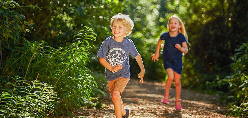 Boy and girl run down forest path in the summer sun