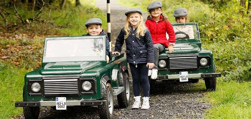 Children riding in two green Off-Road Explorer cars down woodland path