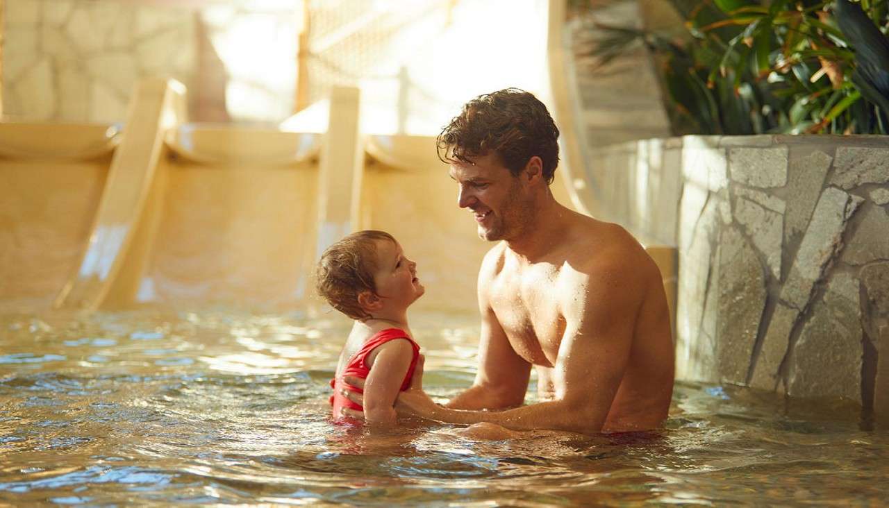 Young boy sitting at the bottom of a water slide, wearing a life jacket.