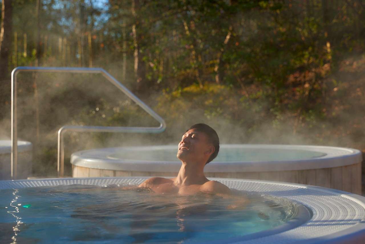 A gentleman relaxing in a outdoor hot tubsurrounded by forest