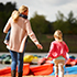 Mother holding a child in her arms and walking on the beach down to the lake with another child by her side