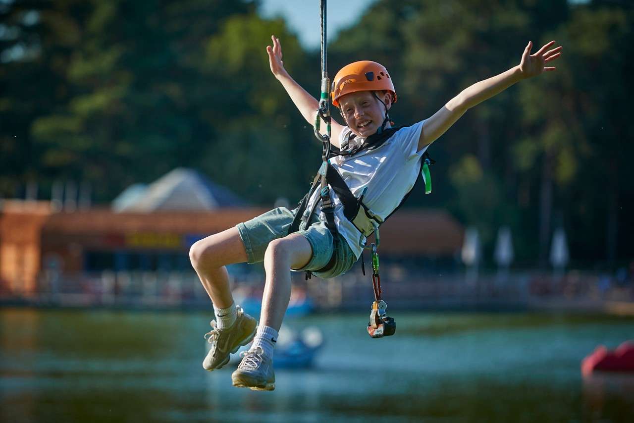 Girl in harness and helmet walking across ropes on Aerial Adventure activity
