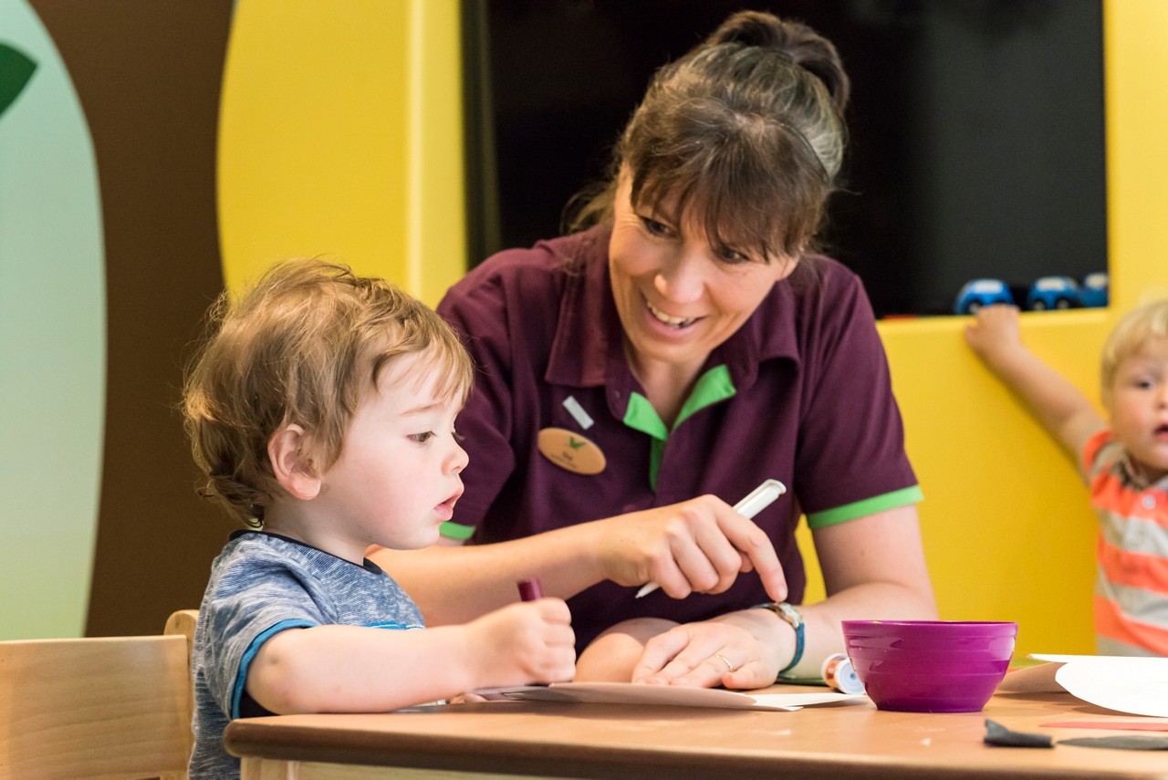 Toddler sitting with an adult making crafts.