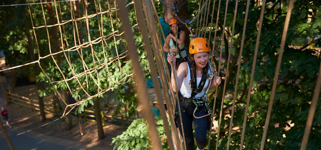 A teenage girl trekking though the trees on ropes