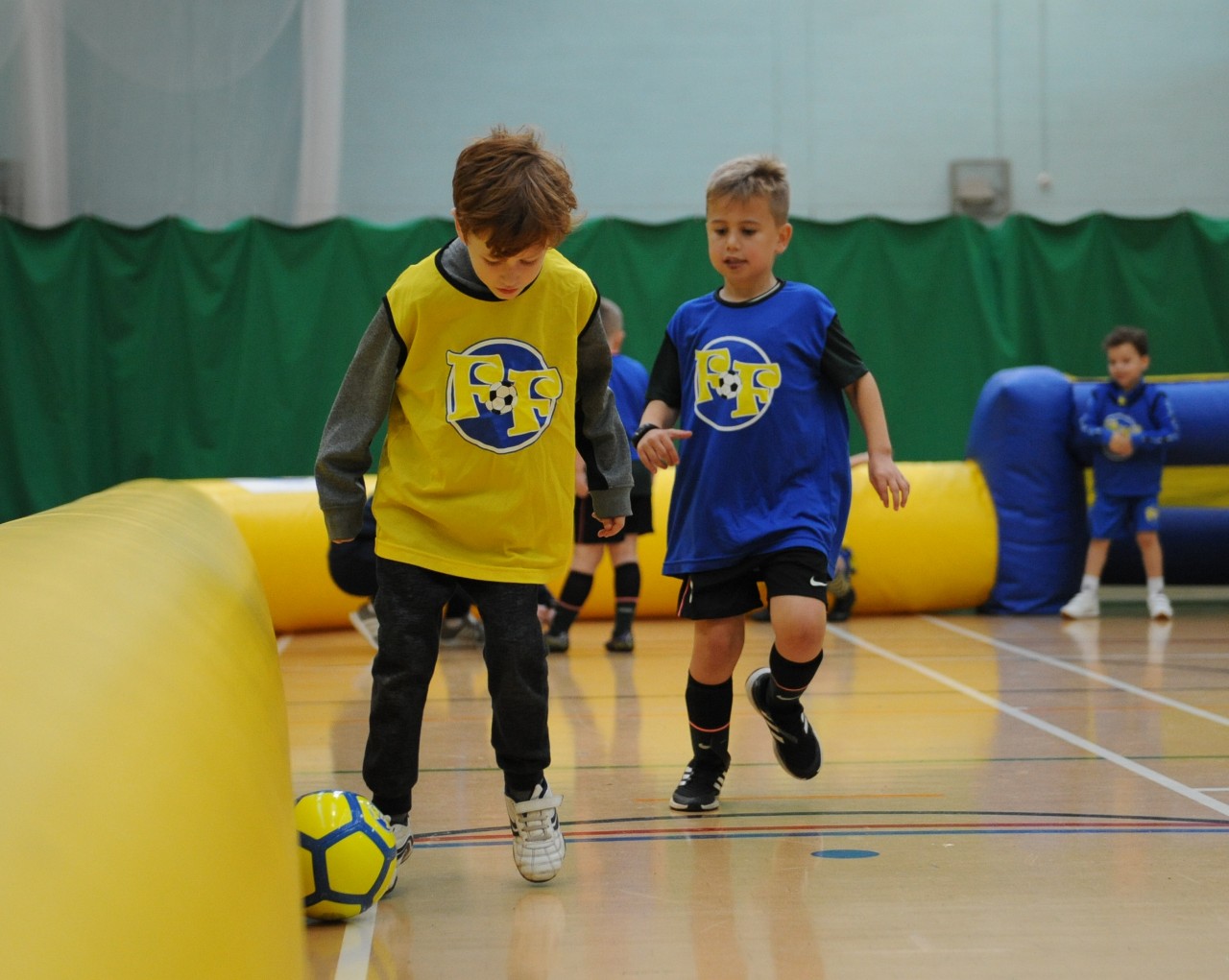 Two young people playing football in a sports hall.