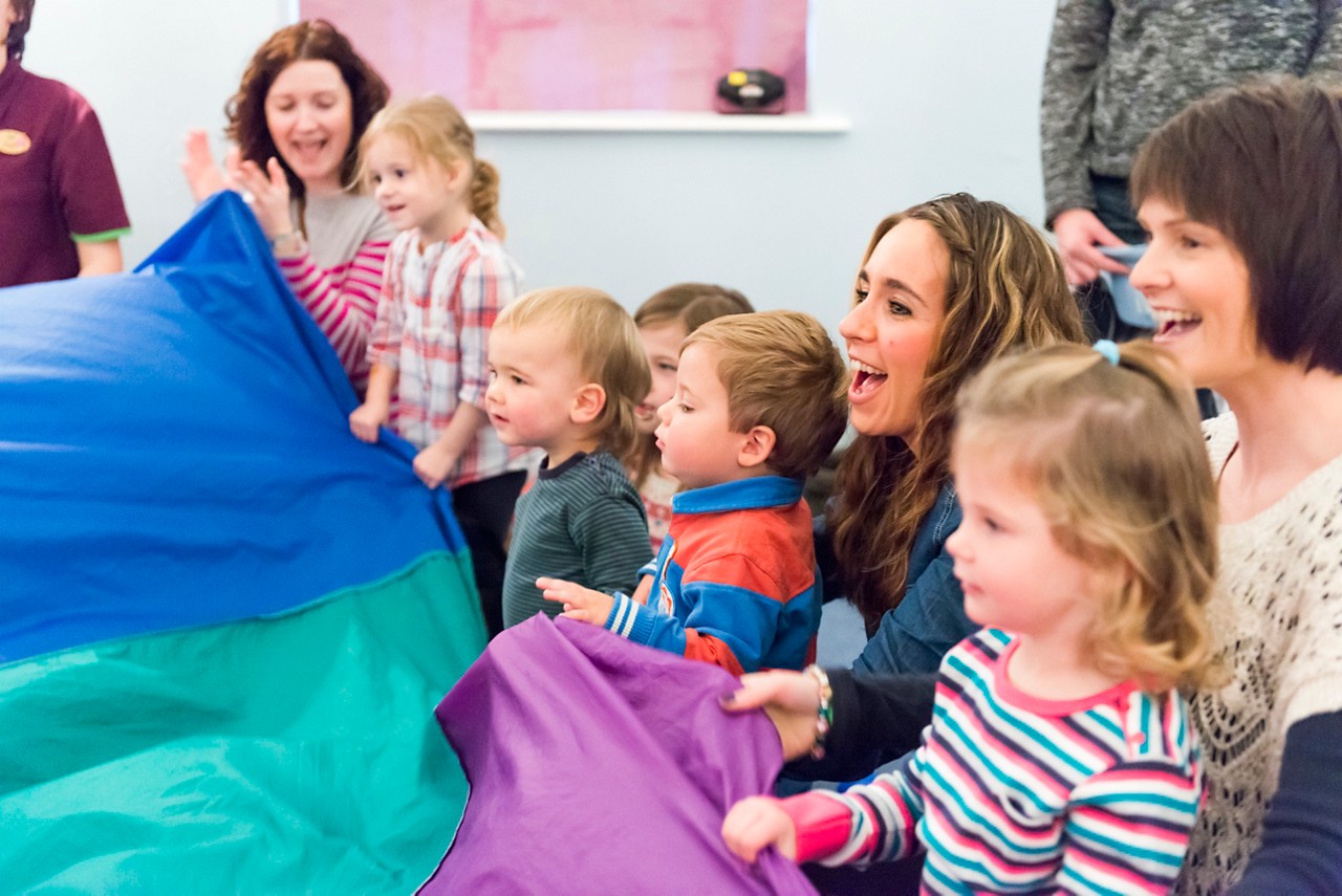 Group of toddlers having some fun with a parachute.