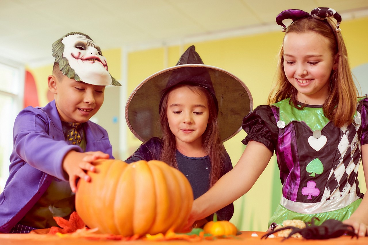 Group of children in fancy dress, looking at a pumpkin.