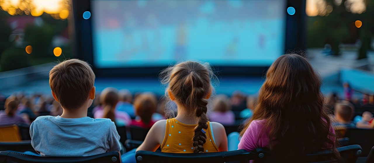 Tree young people sitting watching a movie in an outdoor cinema.