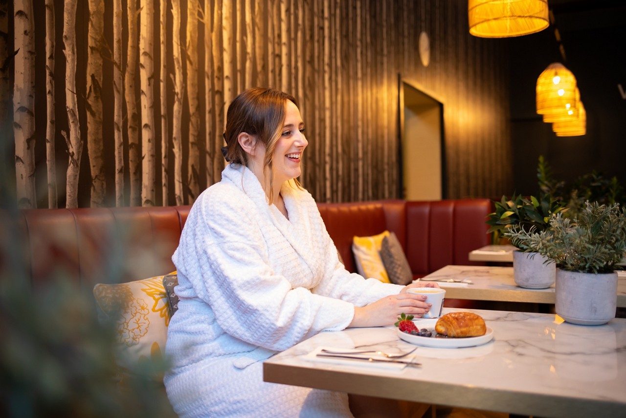 Woman sitting in the Vitalé Café Bar with a hot drink and pastry.