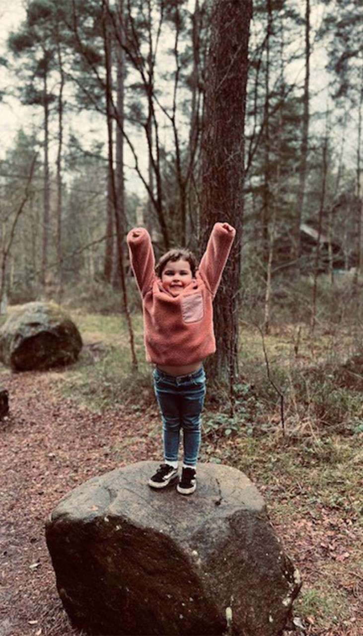 A child stood on a rock in the forest.