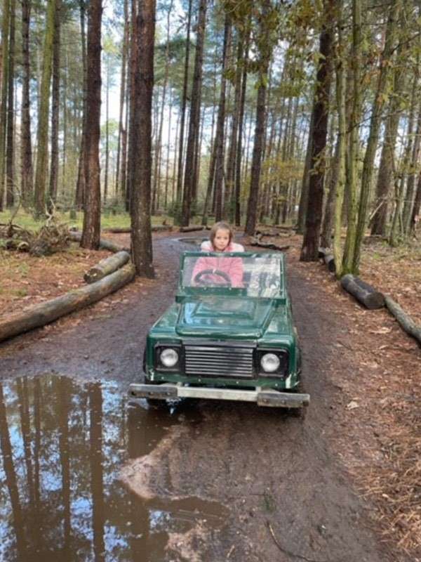 A little girl driving a small off road explorer car through the forest.