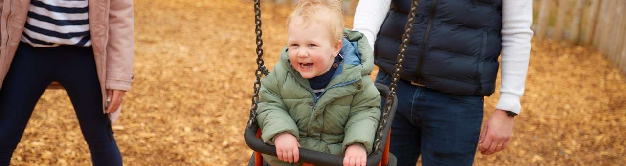 A toddler sat in a swing in an outdoor playground.